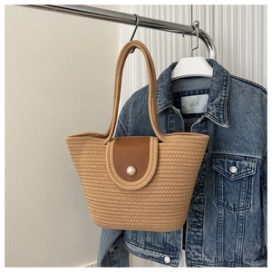 Detail of woven straw tote bag featuring a leather flap and large pearl closure