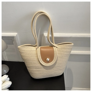 Detail of woven beach tote showing beige texture, pearl button, and brown leather flap
