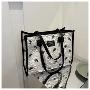 Detail of white quilted tote bag featuring black rose pattern and fashion label