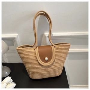Detail of light khaki woven tote bag featuring a brown leather flap with white pearl buckle