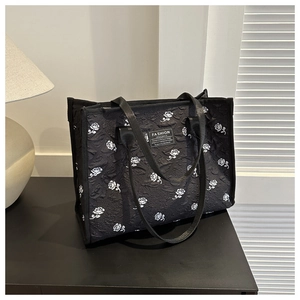 Detail of black tote bag featuring white rose prints and textured embossed fabric surface
