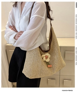 Détail d'un sac cabas en paille tissée avec breloque fleur 3D et anses en cuir brun