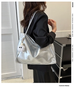Macro detail of silver metallic tote bag featuring mirror PU leather and plush monster charm