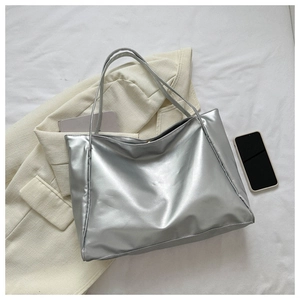 Flat lay of a silver metallic tote bag on a beige blazer with a phone and a notebook