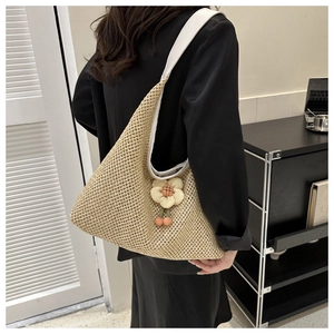 Détail du sac cabas en paille tissée avec breloque fleurie et bandoulière blanche