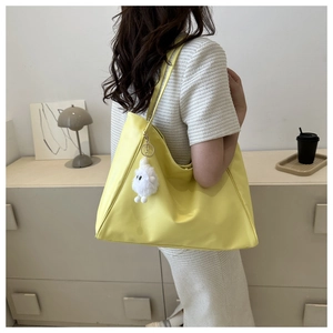 Bright yellow large tote bag with plush monster charm worn by model in home setting