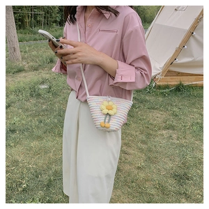 Outdoor model wearing a straw crossbody bag with yellow flower detail and pom-poms