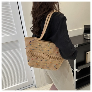 Détail du sac fourre-tout en paille tissé main avec pompons colorés et texture ondulée