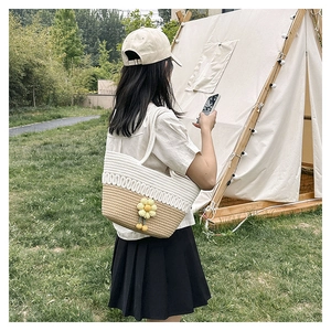 Detail of hollow woven cotton bag with yellow floral pendant and pom-poms for beach