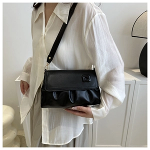 Détail du sac bandoulière noir avec texture plissée et boucle carrée porté par le mannequin