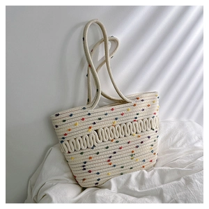 Detail of woven straw tote bag with colorful pom-poms and textured rope patterns