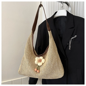 Détail d'un sac cabas tissé beige avec bandoulière en cuir et breloque fleurie