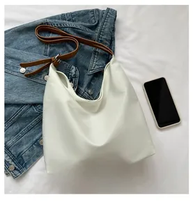 Detailed top view of large white leather tote bag with brown strap on denim jacket