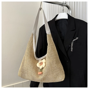 Détail d'un sac hobo tressé beige avec bandoulière blanche et pendentif fleur rose