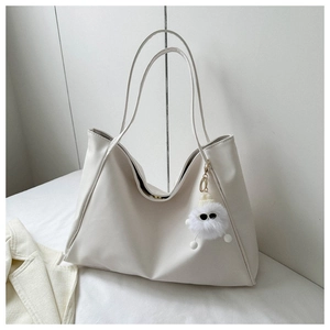 Detail of white leather tote bag featuring a cute plush monster charm and sleek straps