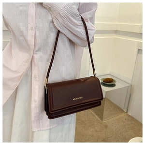Detail of a dark brown leather crossbody bag with a gold brand logo on white background
