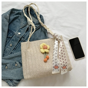 Flat lay of beige straw tote bag with yellow flower charm and silk scarf handle detail