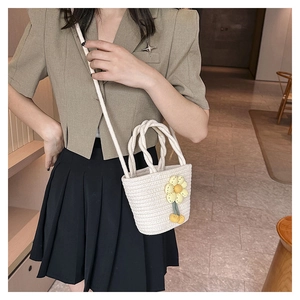 Detail of straw woven bucket bag featuring floral charm and dual carrying straps