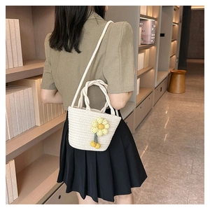 Detail of a white woven bucket bag featuring a yellow knitted flower and tassel accessory