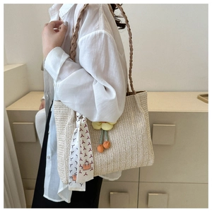 Detail of cream woven tote bag with brown straps, floral charm, and printed scarf