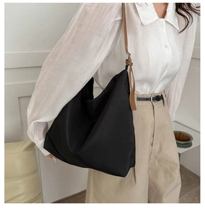 Detail view of black nylon tote bag with brown leather shoulder straps and metal rings