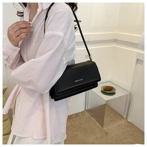 Detail of a black leather rectangular flap shoulder bag with gold logo and long strap