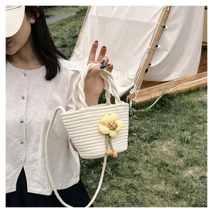 Straw mini bucket bag with yellow flower charm on grass with tent background