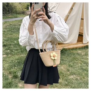 Outdoor view of a woven straw bucket bag with knit flower and tassel details