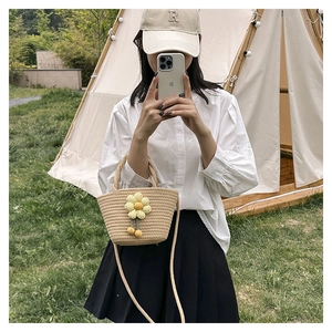 Detail of hand-woven beige straw bucket bag featuring a knit flower and thin shoulder strap