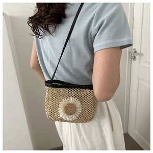 Detail of summer straw crossbody bag featuring large white daisy ornament and black strap