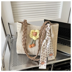 Close-up of beige straw tote bag featuring yellow flower charm and patterned silk scarf