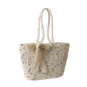 Cream woven tote bag with colorful pom-poms and lace bow detail for summer fashion
