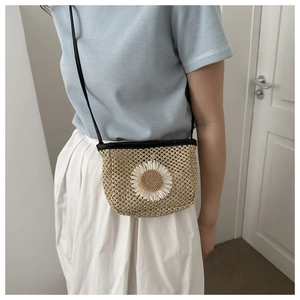 Detail of woven straw mini bag with large white daisy floral charm and black strap