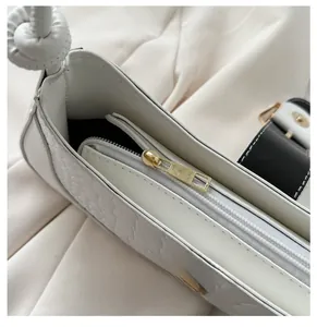 Détail de la fermeture éclair dorée et texture crocodile sur le sac blanc chic