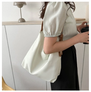 Detail view of a large cream nylon tote bag with brown leather strap on a shoulder