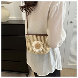 Close-up of woven straw crossbody bucket bag featuring a white daisy flower detail