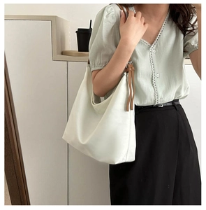 Detail of cream Oxford tote bag featuring brown leather straps and side ribbon accents