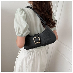 Détail d'un sac baguette noir à motif crocodile avec une boucle dorée sur un mannequin