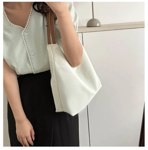 Detail view of cream Oxford tote bag with brown leather straps on woman shoulder