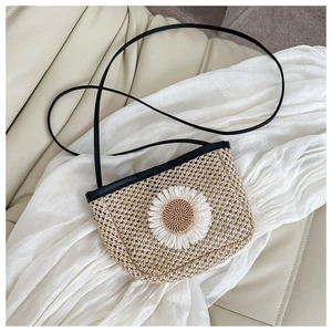 Close-up of woven straw bag featuring a white daisy flower and slim black shoulder strap