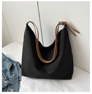 Detail of black nylon tote bag featuring brown leather shoulder straps and metal buckle