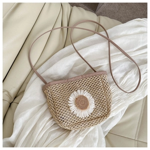 Detailed view of beige woven straw bag featuring white daisy flower and slim leather strap