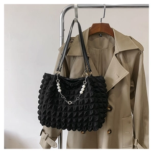 Detail showing the black bubble textured tote bag with a pearl flower charm hanging on a coat