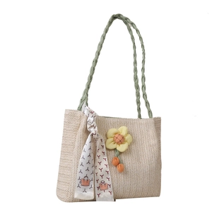 Large woven straw tote bag in light beige with green handles and floral charm