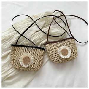 Detail of hand-woven straw crossbody bag featuring a white daisy and textured finish