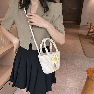 Cream woven straw bucket bag with yellow flower charm and crossbody strap for beach