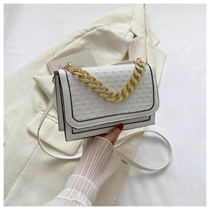 Detail of white woven crossbody bag with decorative gold chain and black edge contrast