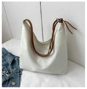 Detail of a minimalist off-white tote bag with brown straps and soft leather texture