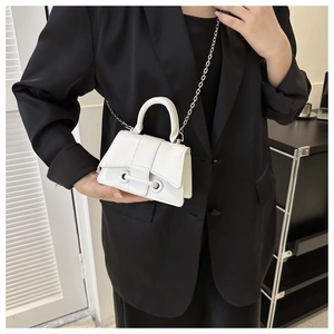 Close-up of a white minimalist handbag with curved bottom and chain strap on a black blazer