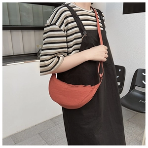 Model wearing orange nylon dumpling crossbody bag with wide shoulder strap